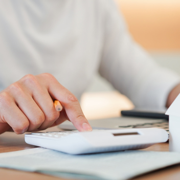 Person typing into calculator and laptop with a small model house next to them